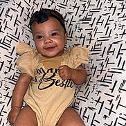 Avani is registered to the contest to win money with this photo: baby, infant, smiling, face, headband, clothing, onesie, patterned_background, cushion, person, cute, happy, skin, fist, sitting, indoors, child, young, comfortable, portrait