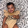 baby, infant, smiling, face, headband, clothing, onesie, patterned_background, cushion, person, cute, happy, skin, fist, sitting, indoors, child, young, comfortable, portrait