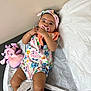 baby, infant, pacifier, onesie, headband, plush_toy, toy, lying_down, curious, indoors, fabric, skin, hand, face, cute, child, soft_surface, colorful_clothing, expression, young