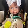 baby, child, car_seat, white_bow, plush_toy, blue_eyes, face, clothing, toddler, infant, cute, portrait, soft_toy, seatbelt, indoor, person, headwear, expression, closeup, seat