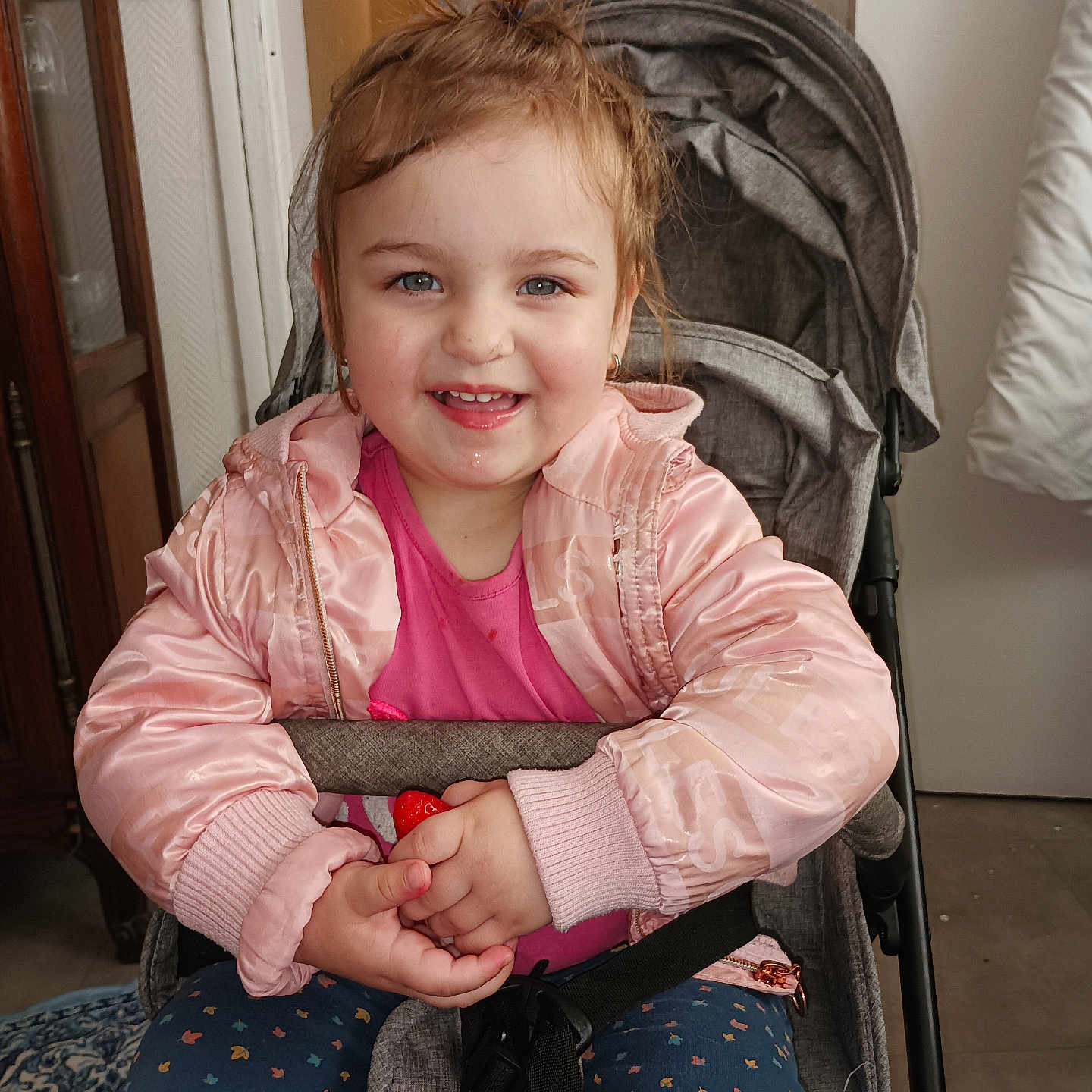 Sofia Cataleia a rejoint le concours — aidez-le/la à gagner de superbes lots ! blue_eyes, carpet, child, clothing, door, drool, face, hair_tied_up, hands, happy, indoor, patterned_pants, person, pink_jacket, seatbelt, smiling, stroller, toddler, toy, wooden_furniture