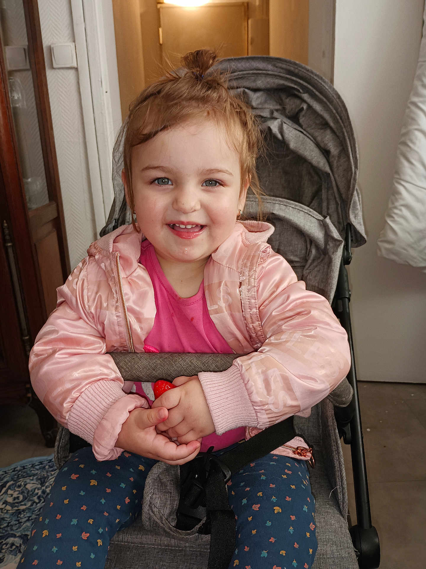 Sofia Cataleia a rejoint le concours — aidez-le/la à gagner de superbes lots ! blue_eyes, carpet, child, clothing, door, drool, face, hair_tied_up, hands, happy, indoor, patterned_pants, person, pink_jacket, seatbelt, smiling, stroller, toddler, toy, wooden_furniture