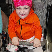 Sofia Cataleia a rejoint le concours — aidez-le/la à gagner de superbes lots ! baby, blue_eyes, child, clothing, curly_hair, cute, fabric, grip, headband, indoor, orange_hoodie, person, pink_bow, playful_expression, seated, skirt, smile, stroller, toddler, white_tights