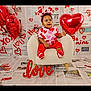 baby, balloon, child, decoration, festive, headband, heart_balloon, heart_pattern_clothing, love_sign, newspaper_background, plush_chair, portrait, props, red_color, sitting, smiling, socks, studio_shot, toddler, valentine_theme