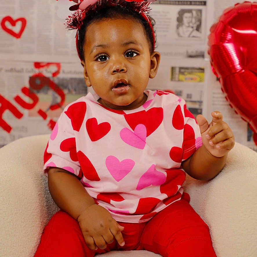 Zanari is registered to the contest to win money with this photo: accessory, baby, balloon, celebration, chair, child, cute, expression, headband, hearts, holiday_theme, newspaper_backdrop, outfit, patterned_shirt, pink_and_red, portrait, sitting, studio_background, toddler, valentine