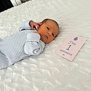 Ibrahim participe au concours pour gagner de l'argent avec cette photo : newborn, baby, infant, lying_down, blue_clothing, striped_onesie, white_blanket, milestone_card, face, head, hand, soft_texture, bedroom, indoor, cute, young_child, skin, sleepwear, resting, portrait