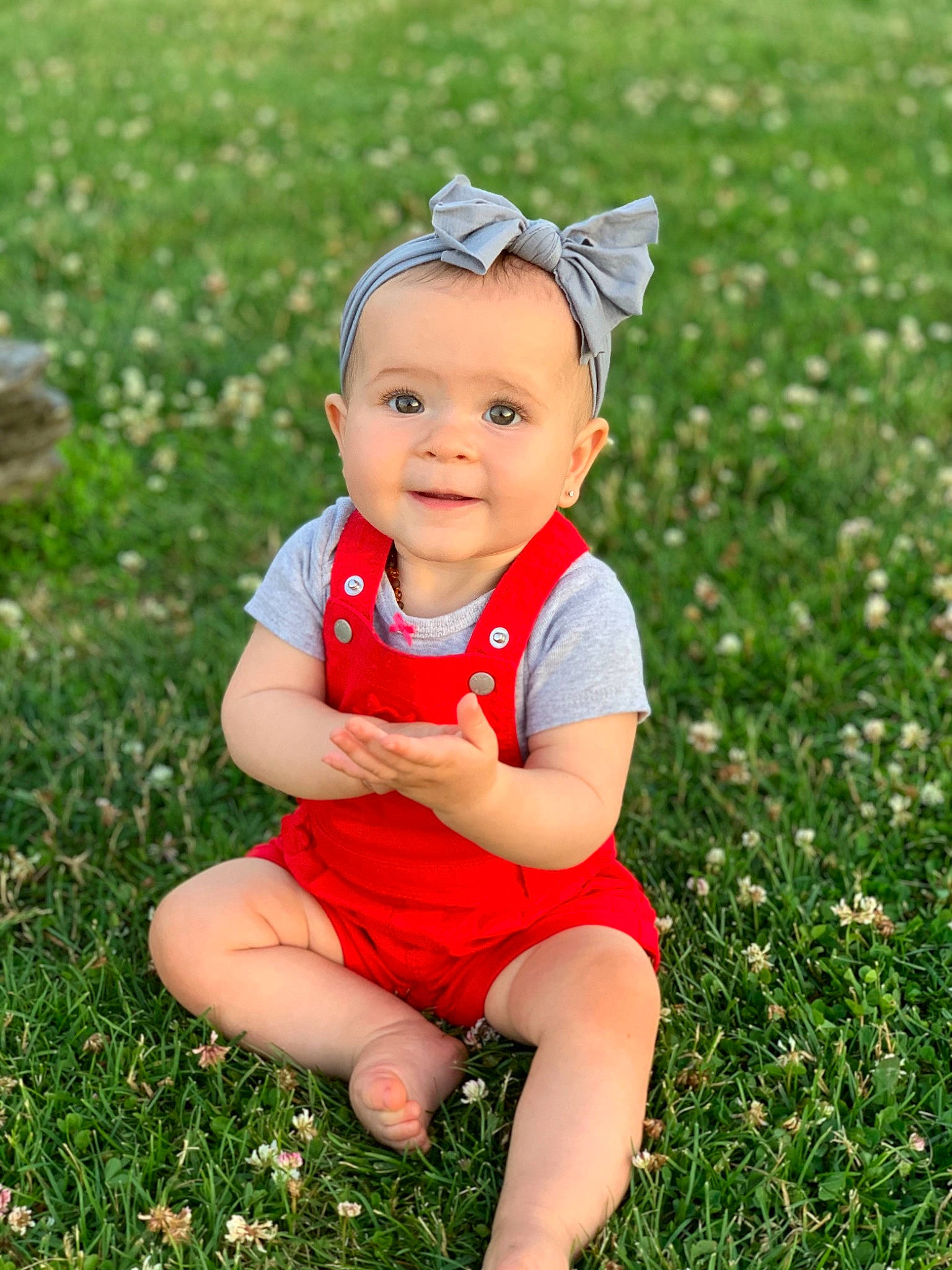 Mariella is registered to the contest to win money with this photo: baby, child, facial_expression, grass, grass_family, happy, head, headgear, joy, lawn, meadow, people, person, photography, plant, red, sitting, skin, smile, spring