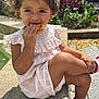 child, girl, curly_hair, pink_dress, sandals, pastry, outdoor, sunlight, flowers, greenery, sitting, cross_legged, face, food, nature, daylight, garden, cute, casual, summer