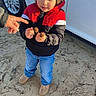 child, boy, jacket, red, black, blue_jeans, shoes, car, white_car, hand, seed_pods, outdoor, sand, curious, standing, person, nature, daylight, casual_clothing, young