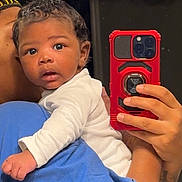 Loyal joined the competition — help win amazing prizes! baby, infant, child, mirror, selfie, phone, red_phone_case, adult_hand, blue_shirt, white_onesie, curly_hair, indoor, portrait, closeup, looking_at_camera, holding, human, skin, face, expression