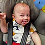 baby, car_seat, child, face, tongue_out, playful, smiling, clothing, seatbelt, infant, red_pants, white_shirt, patterned_shirt, toy, colorful, expression, cute, indoor, closeup, cheeky
