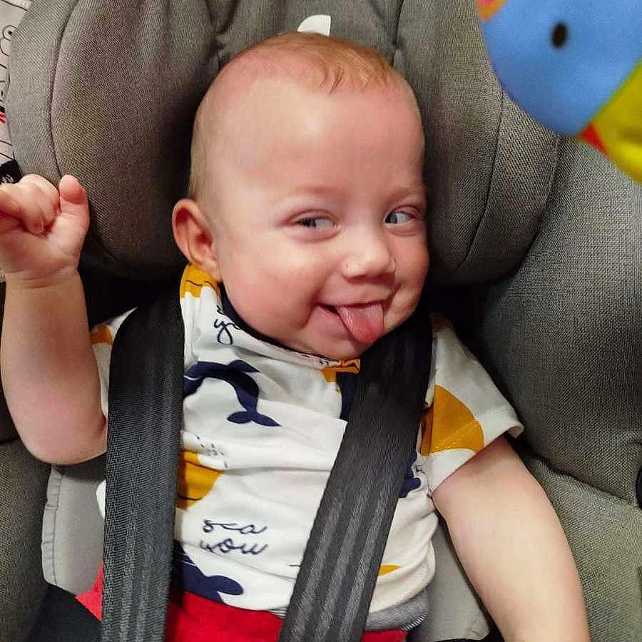 Antonio participe au concours pour gagner de l'argent avec cette photo : baby, car_seat, cheeky, child, closeup, clothing, colorful, cute, expression, face, indoor, infant, patterned_shirt, playful, red_pants, seatbelt, smiling, tongue_out, toy, white_shirt
