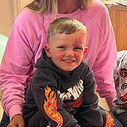 Jax is registered to the contest to win money with this photo: child, boy, smiling, hoodie, flame_design, woman, pink_sweatshirt, indoor, casual, seated, portrait, happy, person, clothing, hair, face, family, toddler, cute, warm_lighting