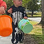 bucket, candy, casual, child, costume, daytime, fall, fun, grass, holiday, nature, outdoor, person, play, shoes, sidewalk, skeleton, toddler, trees, young_child