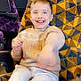 child, smiling, seat, patterned_fabric, yellow, blue, purple_seats, window, snack, clothing, sweater, pants, indoor, public_transport, happy, motion_blur, person, young_child, food, bag