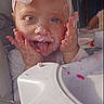 baby, cake, celebration, child, clothing, cute, face, feeding, frosting, hands, happy, headband, high_chair, indoor, infant, messy_face, person, pink_bow, smiling, tongue_out