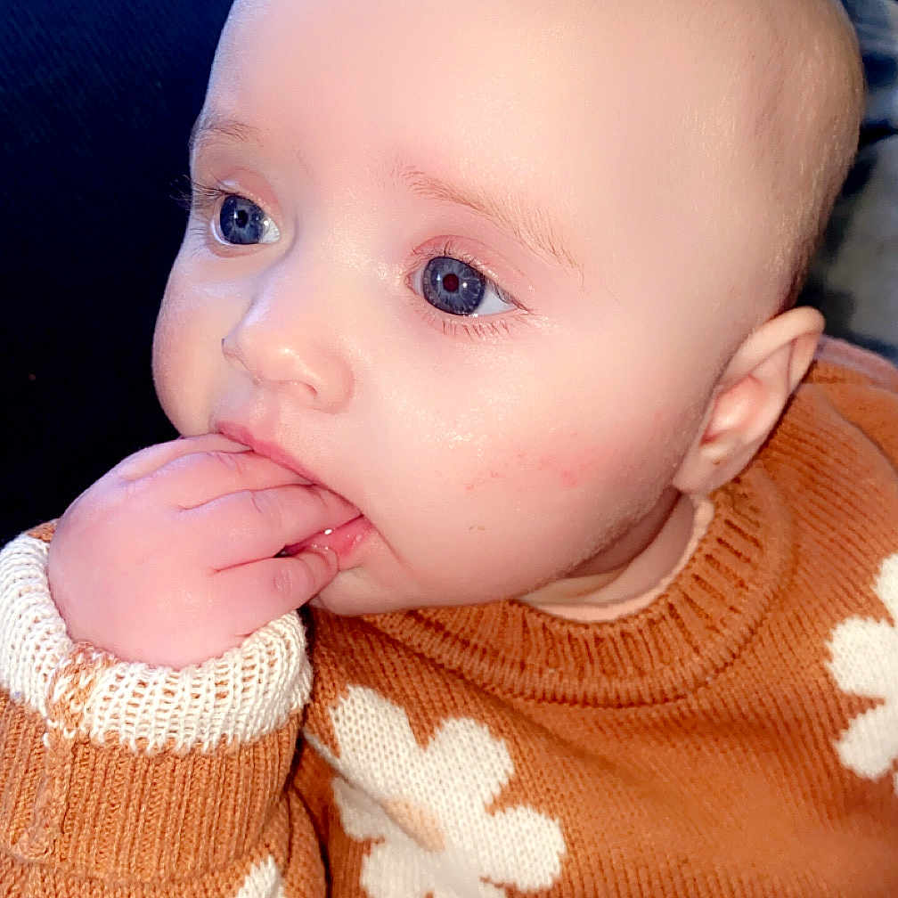 Alaiah Seddon is registered to the contest to win money with this photo: baby, blue_eyes, child, closeup, clothing, cozy, cute, expression, face, fingers, flower_pattern, hand, indoor, infant, portrait, sitting, skin, soft_light, sweater, thoughtful