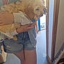 Charlie is registered to the contest to win money with this photo: puppy, dog, person, denim_shorts, jacket, sneakers, indoor, doorway, holding, fluffy, casual_clothing, light, concrete_floor, legs, hand, pet, companion, warmth, candid, comfort