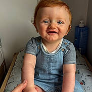 Marceau participe au concours pour gagner de l'argent avec cette photo : baby, blue_eyes, changing_pad, child, cute, denim_overalls, hand, happy, holding_hand, home, indoor, infant, lotion_bottle, person, portrait, red_hair, sitting, skin, smiling, striped_shirt