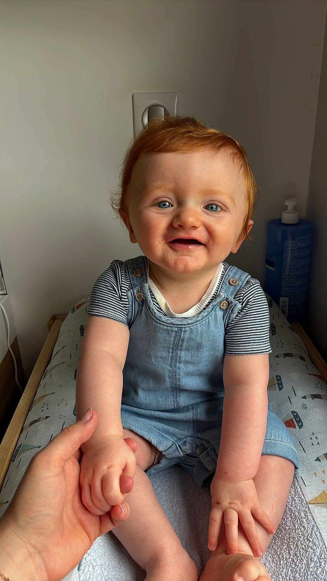 Marceau participe au concours pour gagner de l'argent avec cette photo : baby, blue_eyes, changing_pad, child, cute, denim_overalls, hand, happy, holding_hand, home, indoor, infant, lotion_bottle, person, portrait, red_hair, sitting, skin, smiling, striped_shirt