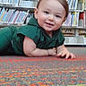 toddler, child, smile, library, bookshelf, carpet, indoors, green_clothing, white_shoes, floor, person, young_child, cute, happy, playful, reading_area, furniture, window, daylight, sitting