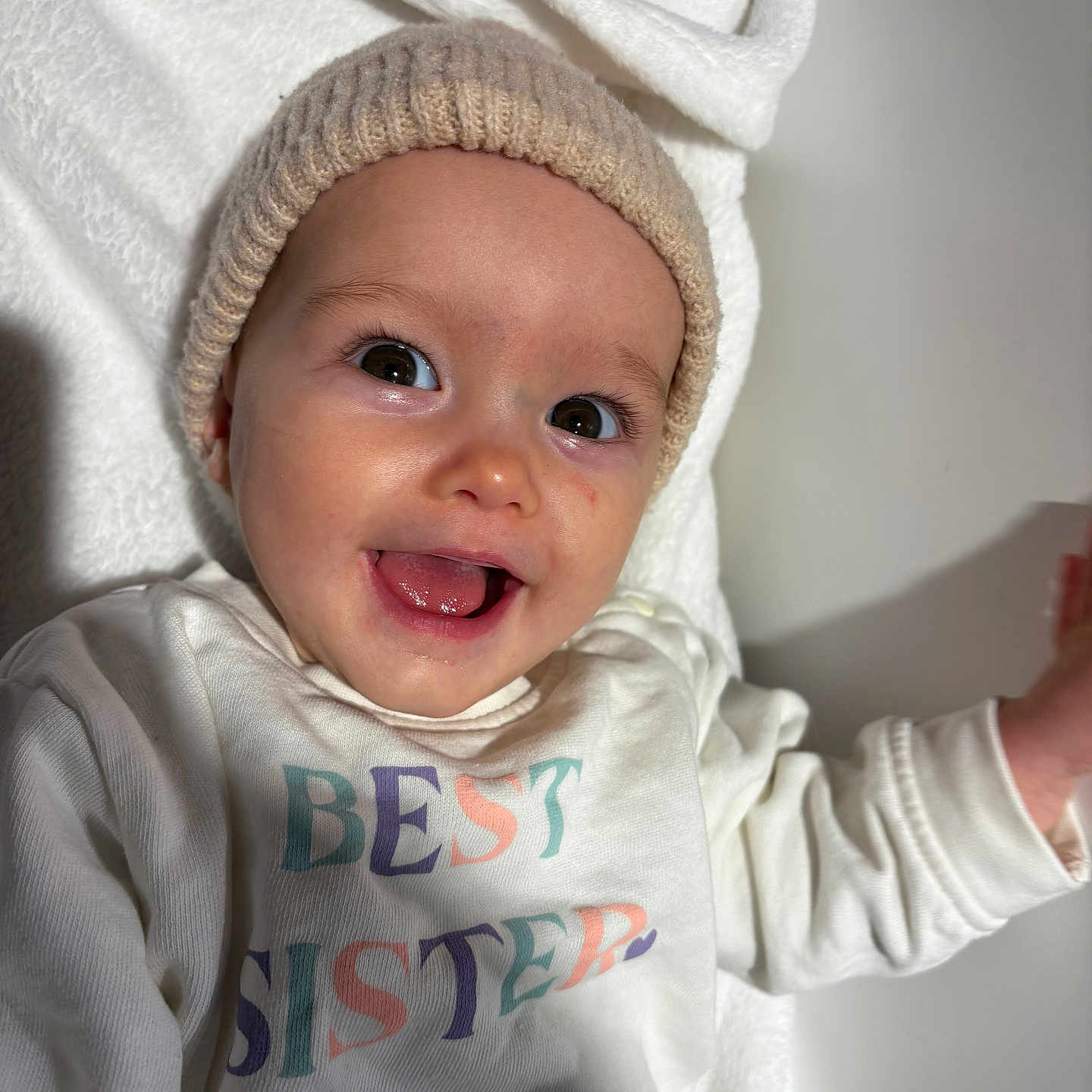 Mylie participe au concours pour gagner de l'argent avec cette photo : baby, best_sister, blanket, child, close_up, cute, eyes, face, happy, hat, indoors, infant, knit_hat, person, portrait, smiling, soft_texture, text_on_clothing, tongue_out, white_shirt