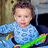 toddler, child, curly_hair, blue_eyes, smiling, playing, toy, green_toy, blue_shirt, football_print, indoor, baby_walker, happy, cute, person, face, hand, clothing, young_child, portrait