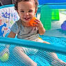 Madden is registered to the contest to win money with this photo: toddler, child, baby, playpen, ball, curly_hair, smile, happy, indoor, colorful, toy, blue, orange, yellow, mesh, clothing, person, face, sitting, playtime