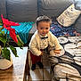 child, toddler, boy, indoor, couch, blanket, pillow, table, plant, poinsettia, clothing, bow_tie, sweater, pants, shoes, tile_floor, smiling, standing, home, portrait