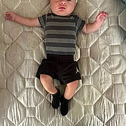 Nio is registered to the contest to win money with this photo: baby, infant, striped_shirt, black_shorts, black_socks, mattress, quilted, bedroom, lying_down, arms_outstretched, legs_crossed, person, child, young, cute, indoors, light_skin, head, face, expression