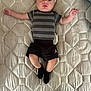 baby, infant, striped_shirt, black_shorts, black_socks, mattress, quilted, bedroom, lying_down, arms_outstretched, legs_crossed, person, child, young, cute, indoors, light_skin, head, face, expression