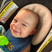 Nio joined the competition — help win amazing prizes! baby, blue_bib, car_seat, child, close_up, comfort, expression, face, green_toy, happy, head, indoor, infant, padded_seat, person, seat_belt, skin, smiling, toy, warning_label