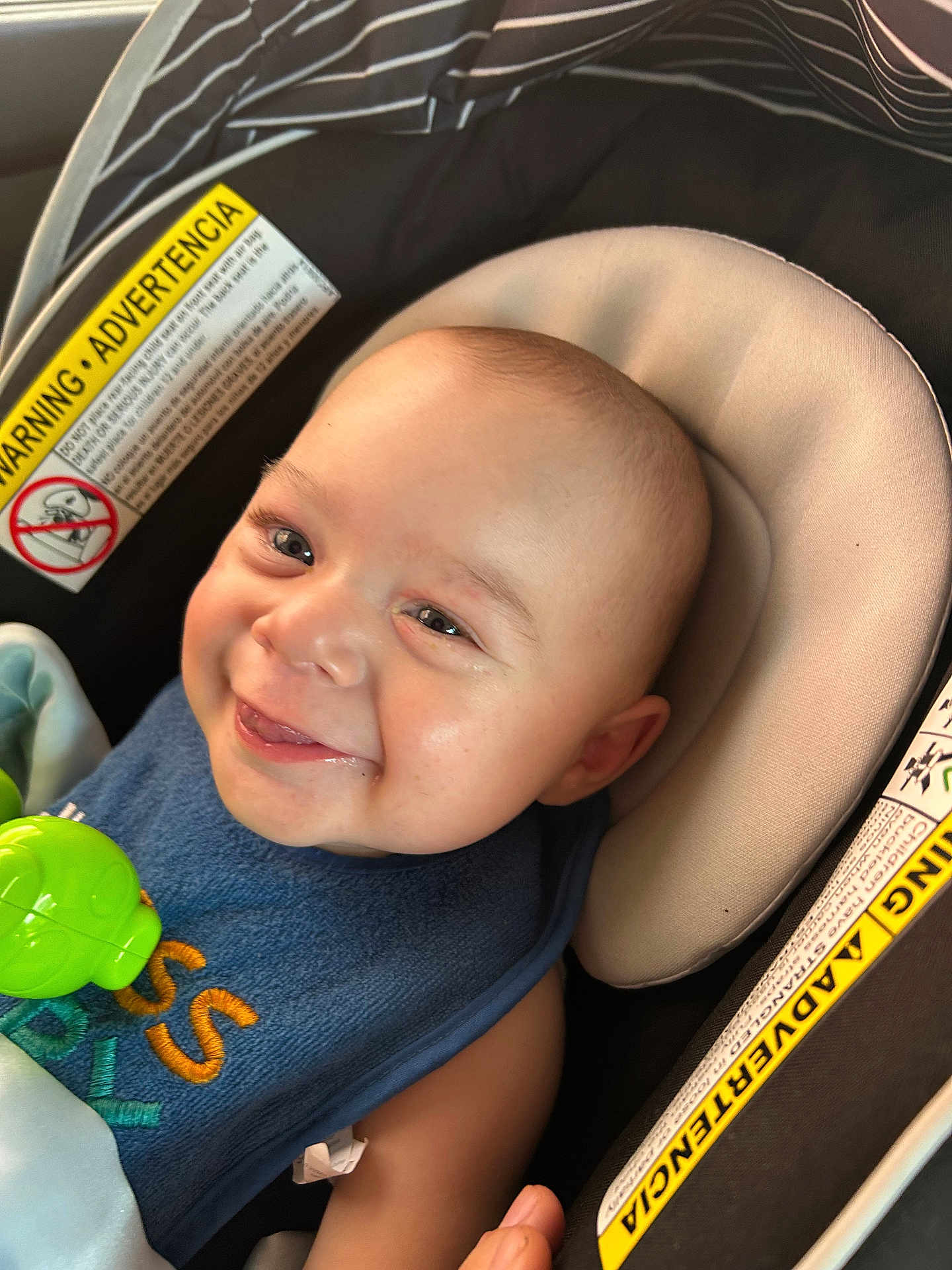 Nio joined the competition — help win amazing prizes! baby, blue_bib, car_seat, child, close_up, comfort, expression, face, green_toy, happy, head, indoor, infant, padded_seat, person, seat_belt, skin, smiling, toy, warning_label