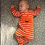baby, sleeping, onesie, orange, white_stripes, pumpkin, star_pattern, blanket, infant, cute, cozy, peaceful, child, footed_pajamas, face, hands_up, lying_down, indoors, soft_fabric, resting