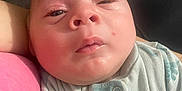 Nio is registered to the contest to win money with this photo: baby, infant, close_up, face, sleepy, onesie, clothing, person, skin, cheek, head, eyelid, mouth, nose, arm, pink_shirt, holding, resting, soft_light, indoor