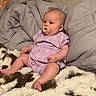baby, infant, pacifier, purple_clothing, blanket, fur_blanket, quilt, bedroom, wall, poster, cute, sitting, child, indoors, comfort, soft, young, person, relax, cozy