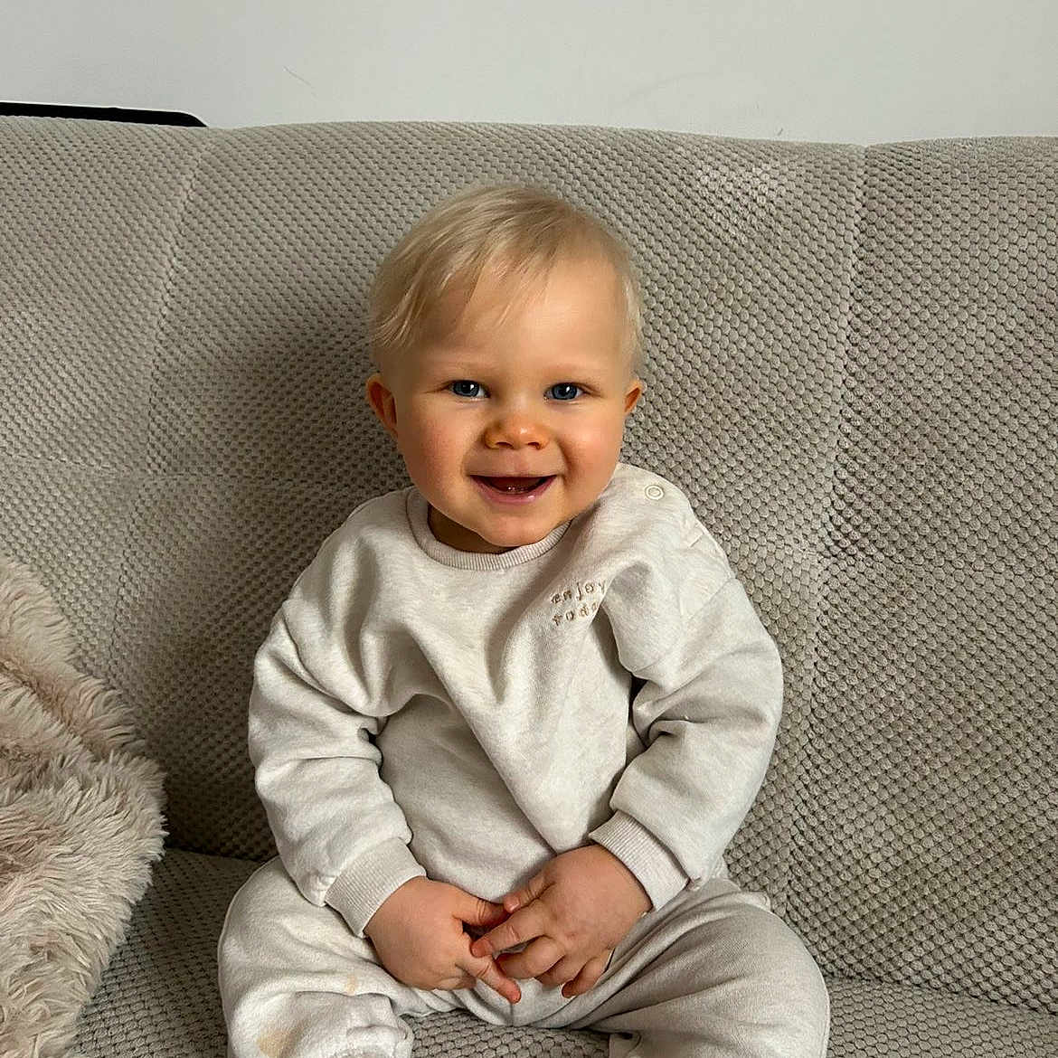 Maylon a rejoint le concours — aidez-le/la à gagner de superbes lots ! baby, blanket, blonde_hair, blue_eyes, couch, cute, hands, happy, indoor, infant, neutral_colors, portrait, seated, smiling, socks, sofa, sweatpants, sweatshirt, textured_fabric, toddler