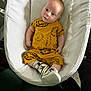 baby, infant, baby_nest, yellow_outfit, lion_print, sneakers, white_texture, baby_bedding, cute, portrait, child, footwear, candid, indoor, soft_light, small_child, comfortable, relaxed, curious, person