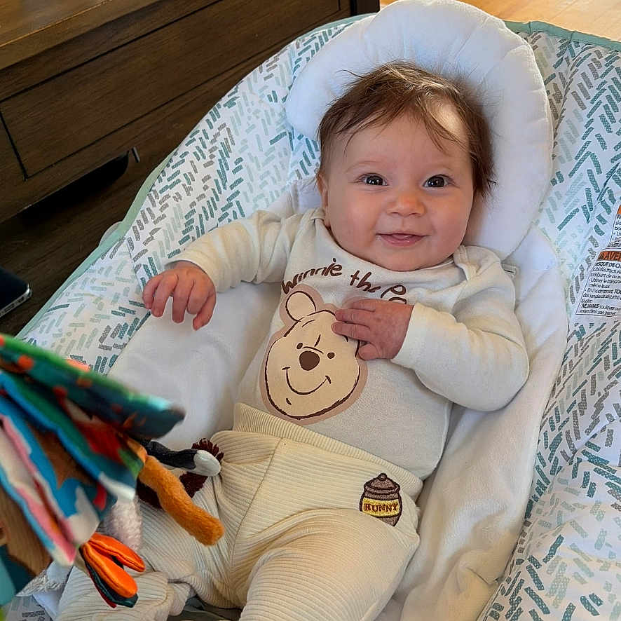 Raelynn joined the competition — help win amazing prizes! baby, infant, smiling, winnie_the_pooh, clothing, toy, cushion, indoor, wood_floor, wood_furniture, face, person, cute, child, happy, seated, playful, cozy, soft_toy, home