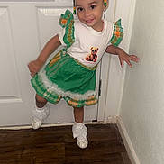 Kay is registered to the contest to win money with this photo: child, girl, smile, dress, green, white, hair_accessories, shoes, socks, door, wall, floor, indoor, pose, happy, cute, fashion, playful, young_child, portrait