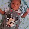 baby, infant, mickey_mouse, clothing, onesie, blanket, lying_down, face, portrait, child, cute, patterned_blanket, red_buttons, white_shirt, expression, looking_at_camera, indoors, soft_lighting, small_child, casual