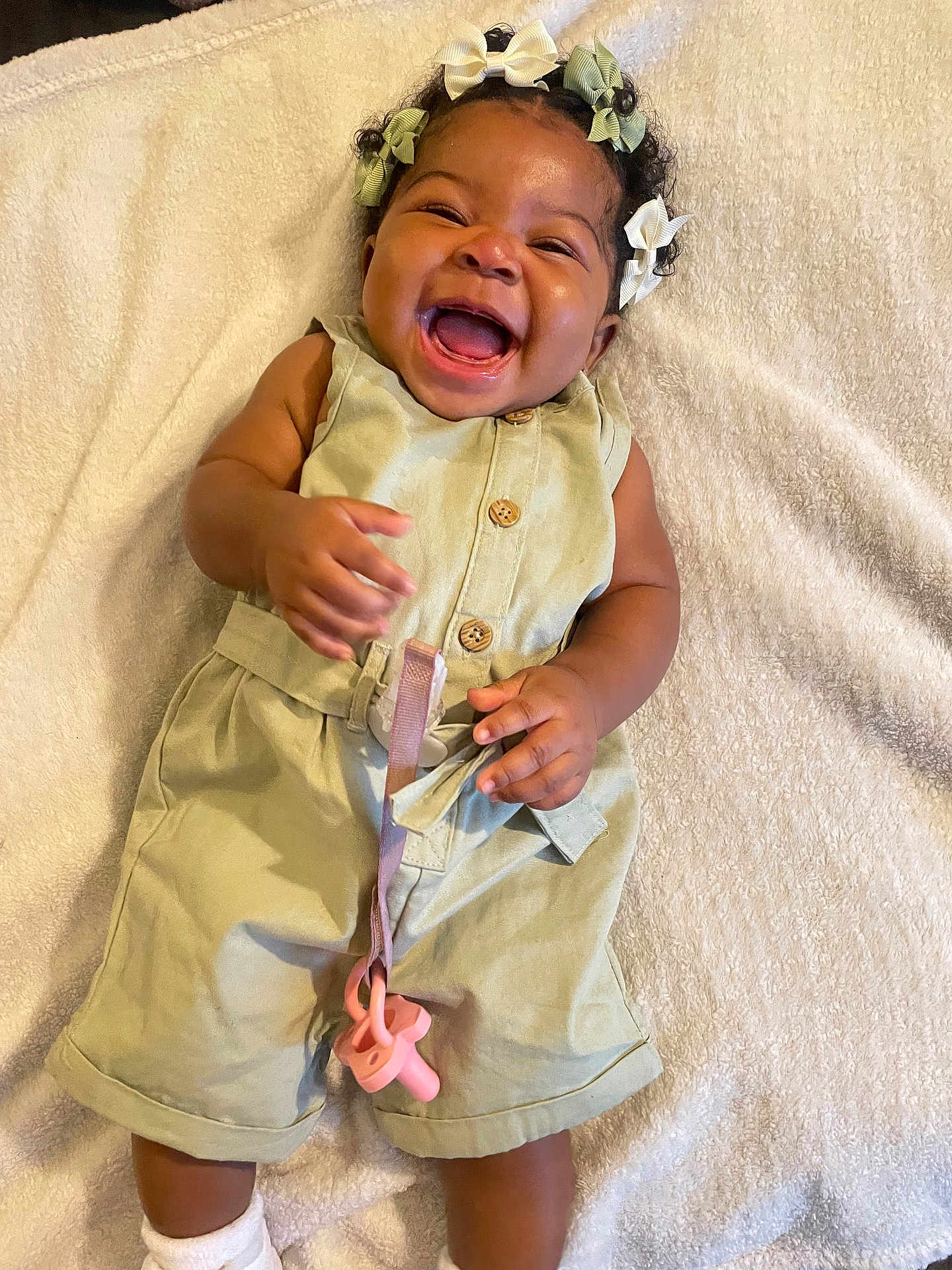 Klani Byrd is registered to the contest to win money with this photo: baby, child, smiling, happy, pacifier, romper, clothing, hair_bows, blanket, infant, cute, joyful, lying_down, skin, hand, feet, toddler, indoors, playful, expression