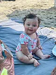 Alena is registered to the contest to win money with this photo: baby, baby_toddler_clothing, body_of_water, cheek, child, fun, grass, hairstyle, happy, head, joy, leisure, person, recreation, sand, sitting, skin, smile, summer, toddler