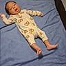 baby, infant, blanket, onesie, pretzel_pattern, playpen, smiling, lying_down, indoors, soft_texture, child, cute, happy, person, foot, hand, head, face, sleepwear, cozy