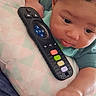 baby, infant, remote_control, pillow, curious, hand, face, eyes, clothing, soft_fabric, indoor, closeup, child, lying_down, colorful_buttons, skin, couch, relaxing, young_child, exploring