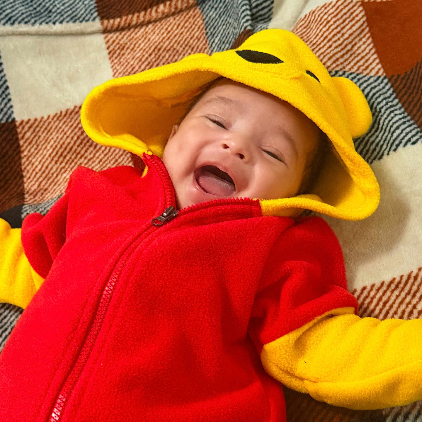 Cristian joined the competition — help win amazing prizes! baby, child, smiling, hood, red_clothing, yellow_clothing, blanket, happy, cute, infant, face, apparel, warm_clothing, patterned_blanket, lying_down, joyful, small_person, indoor, portrait, playful