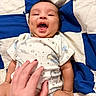 baby, smiling, hand, blanket, blue, white, onesie, infant, happy, toddler, skin, face, lying_down, cute, playful, human, child, tickling, indoors, fabric