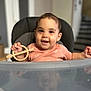 baby, child, high_chair, toy, wooden_toy, smile, face, indoor, reflection, clothing, short_hair, hand, table, curious, cute, infant, person, seat, background_blur, expression