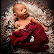 Kristian is registered to the contest to win money with this photo: newborn, baby, sleeping, wrapped, blanket, fur, red_cloth, pendant, hand, face, peaceful, portrait, cozy, resting, infant, soft, closeup, cute, child, indoors