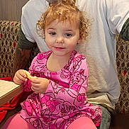 Luna is registered to the contest to win money with this photo: child, toddler, adult, curly_hair, pink_clothing, cartoon_print, sitting, snack, indoor, restaurant, table, jeans, tattoo, beard, long_hair, casual, seat, person, family, relaxing